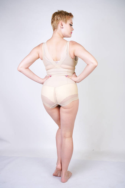 cute chubby girl with short hair and a curvy figure dressed in beige tight shapewear on a white background in the Studio - Foto, imagen
