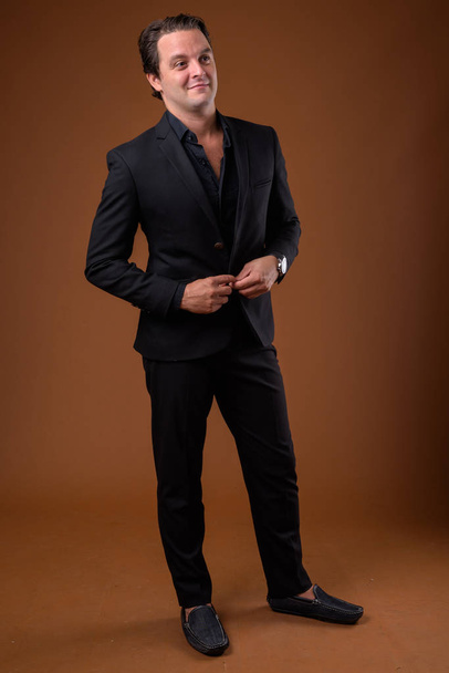 Studio shot of Italian businessman wearing black suit against brown background - Foto, Imagem