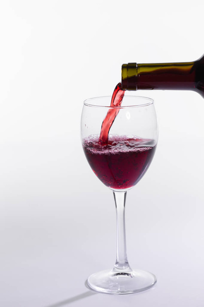 Vino rosso versando da bottiglia in grande vetro su sfondo bianco - Foto, immagini