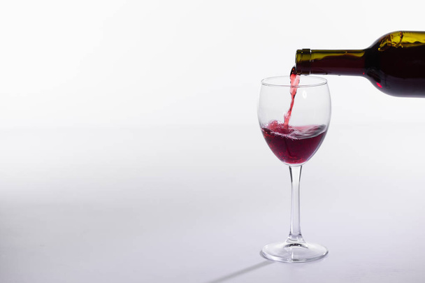 Rode wijn gieten van fles in groot glas op witte achtergrond met Kopieer ruimte - Foto, afbeelding