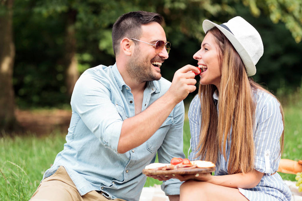 Loving young couple enjoying their time in a park, having a casual romantic picnic - Фото, изображение