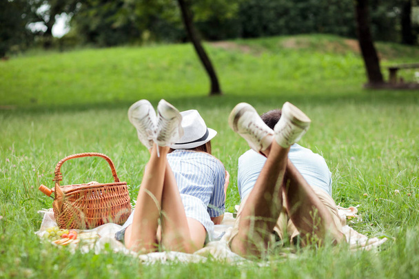 Casal jovem desfrutando de tempo de piquenique relaxante em um parque, deitado em um cobertor de piquenique
 - Foto, Imagem