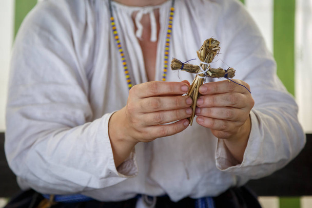 Rus etnik kıyafetli kadın samandan küçük bir oyuncak yapıyor. - Fotoğraf, Görsel