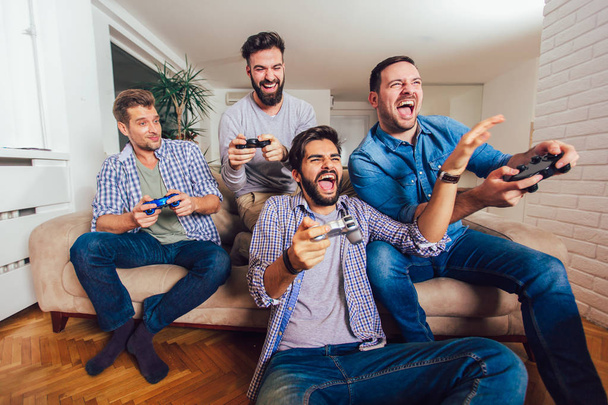 Smiling male friends playing video games at home and having fun. - Photo, image
