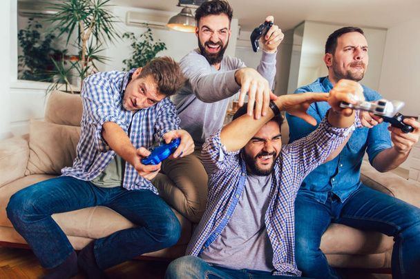 Улыбающиеся друзья-мужчины играют в видеоигры дома и веселятся. - Фото, изображение