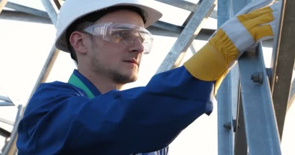An electrician or builder and engineer, in a blue robe, in a yellow and white helmet, check the technical overview for strength, prepare electric poles, an electric tower, energy, and workers. - Séquence, vidéo