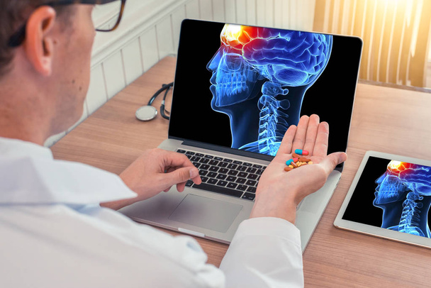 Lääkäri, jolla on pillereitä, joissa on röntgenkuva 3D-kallosta ja kipua aivojen edessä kannettavalla tietokoneella. Digitaalinen tabletti pöydällä
 - Valokuva, kuva