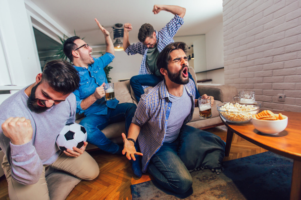 Miehet katsovat urheilua televisiosta yhdessä kotona huutaen iloisesti. ryhmä I
 - Valokuva, kuva