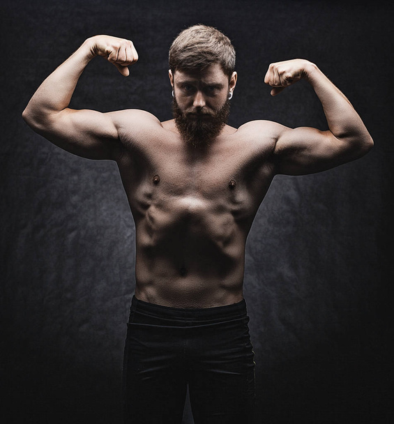 junger starker Mann Bodybuilder auf schwarzem Hintergrund. - Foto, Bild