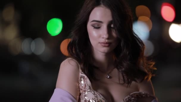 Beautiful attractive woman looking at camera in night city, slow motion - Záběry, video