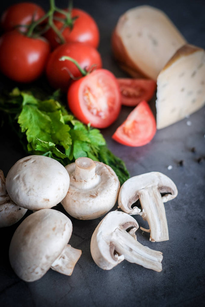 Ingredientes alimentares para pizza sobre fundo preto, como tomates, queijo ou cogumelos
 - Foto, Imagem