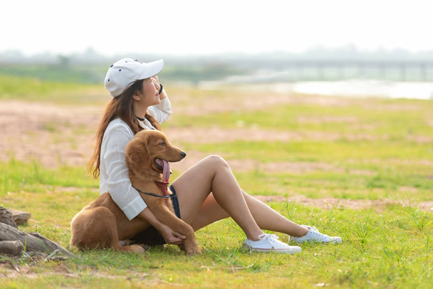 Asian lifestyle woman playing with golden retriever friendship dog in sunrise outdoor the summer park. - Fotoğraf, Görsel