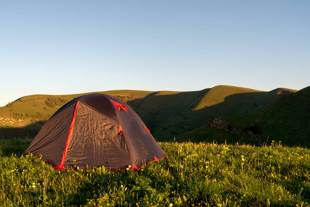 tourist tent stands on the green grass in the morning on a background of mountains - Photo, Image