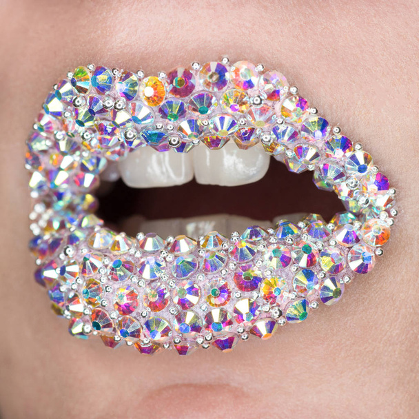 Beautiful closeup with female lips with white colorfull gemstones. Open mouth with white teeth. Make-up, lip art - Photo, image