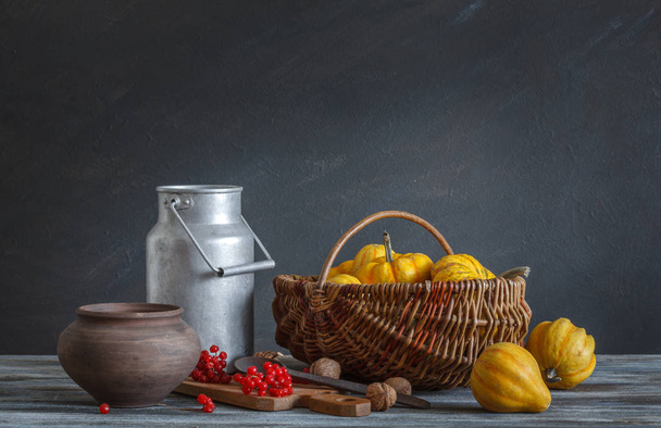Still life in a rustic style: autumn harvest. luminium cookware, pumpkins and red berries on a wooden table. Natural light from a window. - Foto, imagen