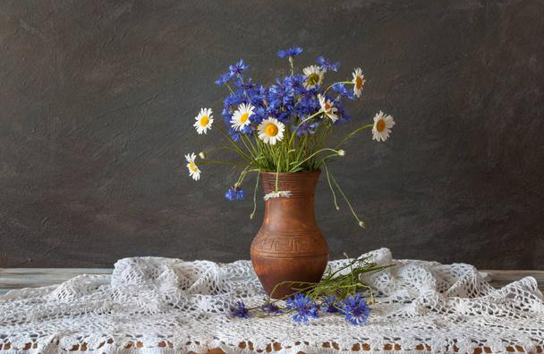 Натюрморт у сільському стилі. Букет з польових квітів у глиняному глечику на столі. Денне світло
. - Фото, зображення