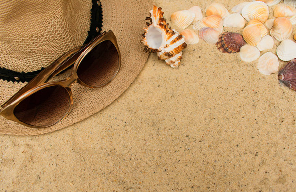 Letnia koncepcja wakacji z muszli, kapelusz plażowy kobiet i okulary przeciwsłoneczne na tle piasku. Płaski lay, widok z góry. Kopiuj przestrzeń - Zdjęcie, obraz