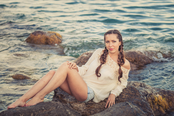 Beautiful young woman sitting on the stone on the seashore - Foto, afbeelding