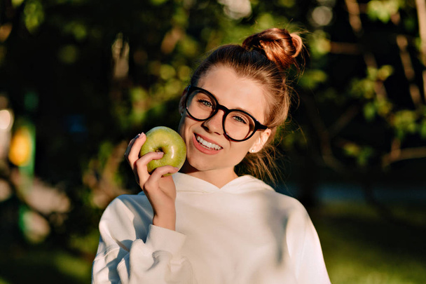Bliska portret uroczy Ładna dama noszenie okulary jedzenia jabłko w słońcu w parku - Zdjęcie, obraz