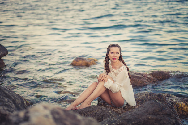 Beautiful young woman sitting on the stone on the seashore - Foto, Bild