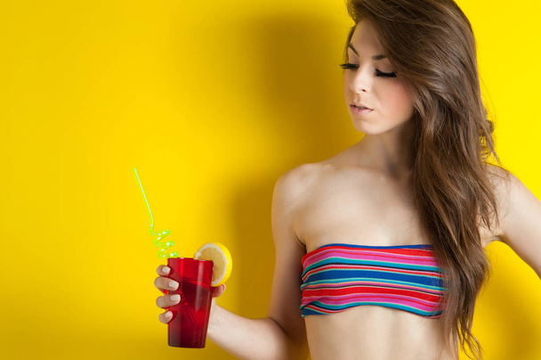 Beautiful girl drinking a cocktail against yellow background with copy space. - Foto, imagen