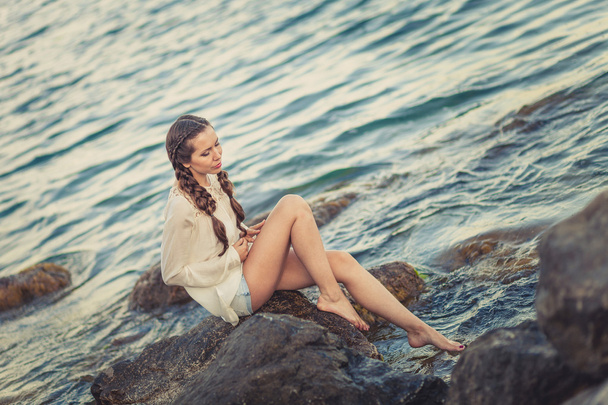 Beautiful young woman sitting on the stone on the seashore - Photo, Image