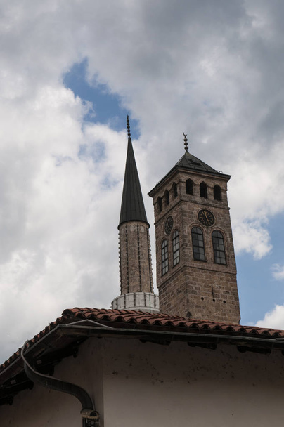 Sarajevo, Bosnia y Herzegovina, 08 / 07 / 2018: vista de la Sarajevska Sahat Kula, la Torre del Reloj construida por Gazi Husrev-beg, gobernador de la zona durante el período otomano, y el minarete de la mezquita Gazi Husrev-beg (1532) en el barrio de Bascarsija
 - Foto, Imagen
