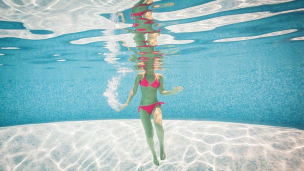 underwater view of girl in pink bikini swimming in pool.  - Zdjęcie, obraz