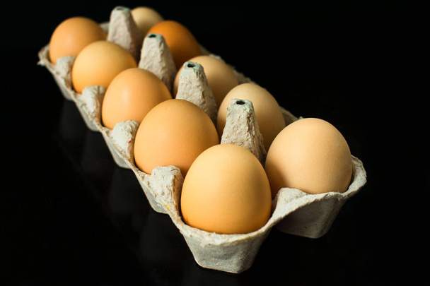 Huevos de gallina en un recipiente de cartón para el almacenamiento y transporte de huevos de gallina aislados sobre fondo negro
 - Foto, imagen