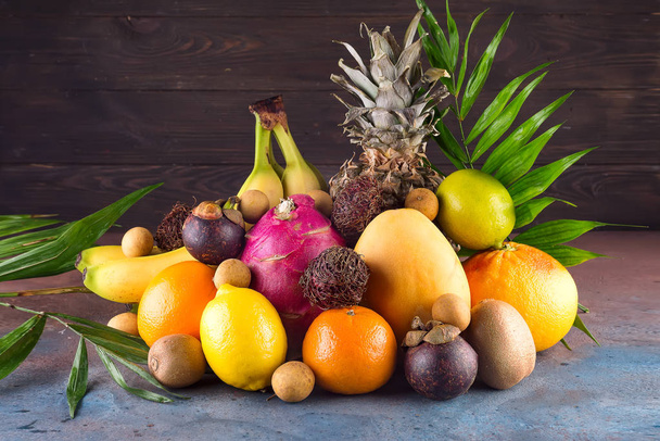 Surtido de frutas exóticas con hojas de palma sobre fondo oscuro
 - Foto, Imagen