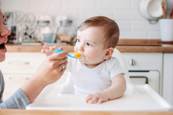 Charmant petit garçon 6-8 mois à manger la première citrouille alimentaire de la cuillère avec maman à la maison
 - Photo, image