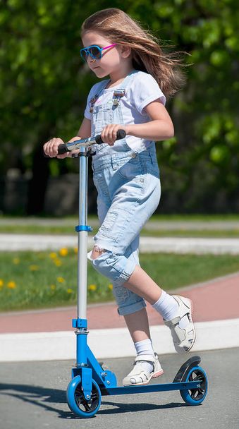 Child riding scooter. Kid on colorful kick board. Active outdoor fun for kids. Summer sports for preschool children. Little happy girl in spring park. The concept of a healthy lifestyle - Fotó, kép