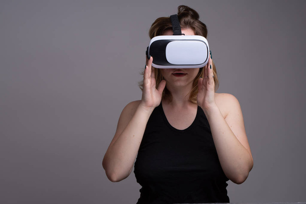 Mujer joven tocando googles VR. Aislado sobre fondo gris
 - Foto, Imagen
