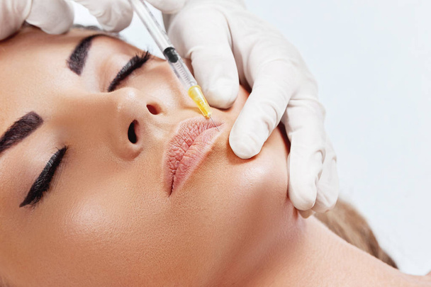 Beautiful woman getting cosmetic injection of botox in lips, Plastic surgery, beauty concept. Closeup hand in glove with syringe making injection. Girl in beauty salon.Hyaluronic Collagen Injection.Facelift - Fotografie, Obrázek