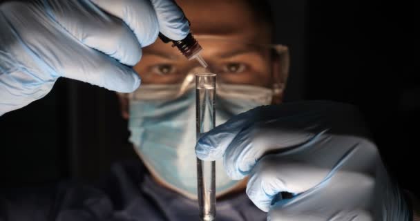 Laboratory worker scientist laboratory assistant tests chemicals for reactions in test tubes, interfering with different substances and obtaining a visual reaction. Male doctor in work uniform wearing gloves with goggles goggles examines in vitro. - Footage, Video