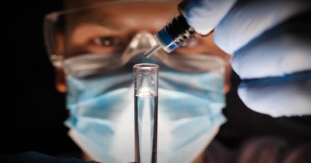 Laboratorní asistent vědec laboratorních pracovníků testuje chemické reakce ve zkumavkách, ruší různé látky a získává vizuální reakci. Mužský lékař v pracovní uniformě nosí rukavice s brýlemi, zkoumá in vitro. - Záběry, video