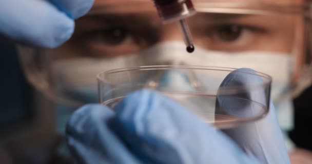 Лабораторный лаборант лаборант проверяет химикаты на реакцию в пробирках, вмешательство в различные вещества и получение визуальной реакции. Мужчина врач в рабочей форме носить перчатки с очками очки обследования in vitro
. - Кадры, видео