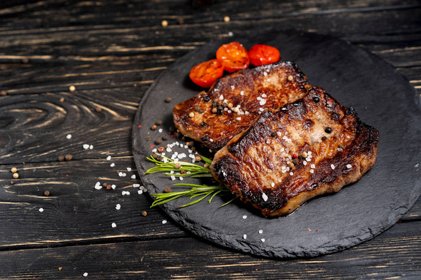 juicy piece of fried meat lies on a stone plate against a black wooden table - Fotoğraf, Görsel