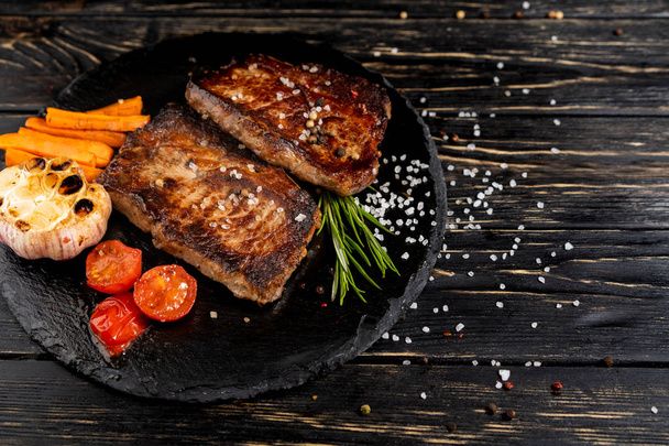 juicy piece of fried meat lies on a stone plate against a black wooden table - Photo, Image