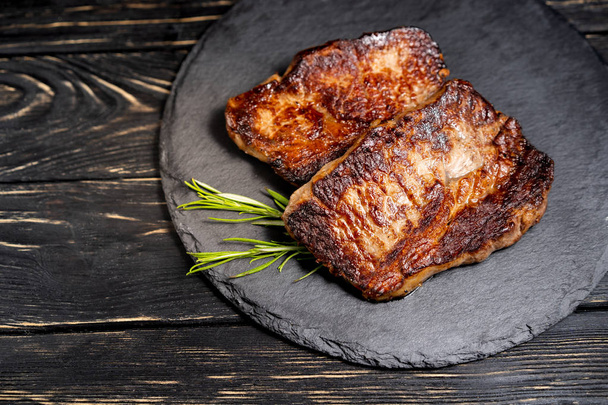 juicy piece of fried meat lies on a stone plate against a black wooden table - Foto, Bild
