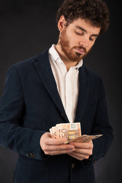 Young man counting euros banknotes against black background. - Fotografie, Obrázek