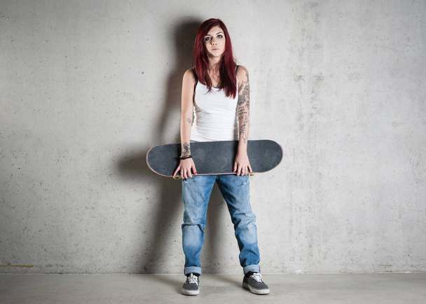 Woman with skateboard full body portrait against concrete wall.  - Photo, Image