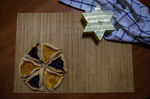 Черничное и абрикосовое печенье Hamantash Purim с деревянным фоном стола и свечой в форме звезды David
 - Фото, изображение
