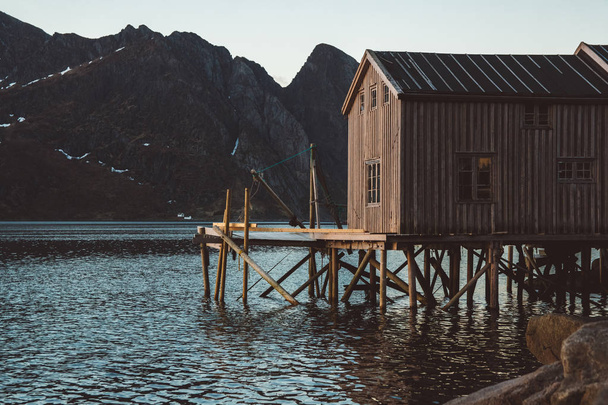 Stare drewniane domy rybackie w pobliżu jeziora na tle gór. Norwegia, Europa. Kopiuj przestrzeń. Może być używany jako baner - Zdjęcie, obraz