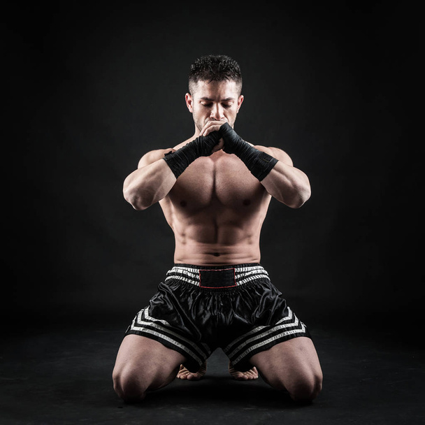 Sportsman kick boxer meditation portrait against black background.  - 写真・画像