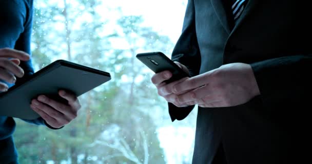 A young guy (Man) businessman in suit is talking holding a telephone in the building (office) on the background of the street waiting for a meeting. Businessman in suit talking holding phone (tablet) in building. - Imágenes, Vídeo