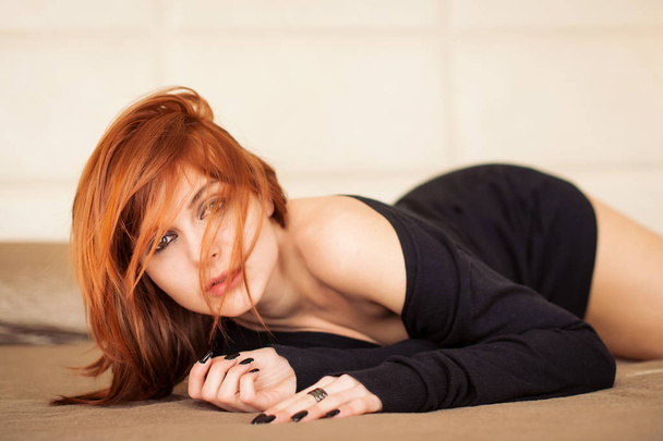 Sensual young red head woman portrait while lying on bed in hotel room. Shallow depth of field.  - Foto, afbeelding