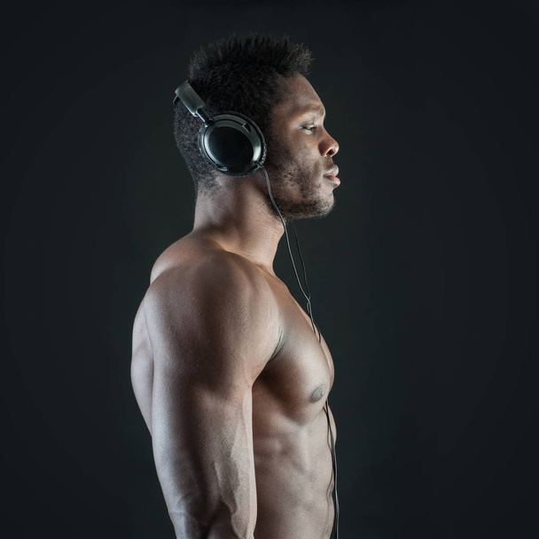 Black man with ear-phones against dark background.  - Фото, зображення