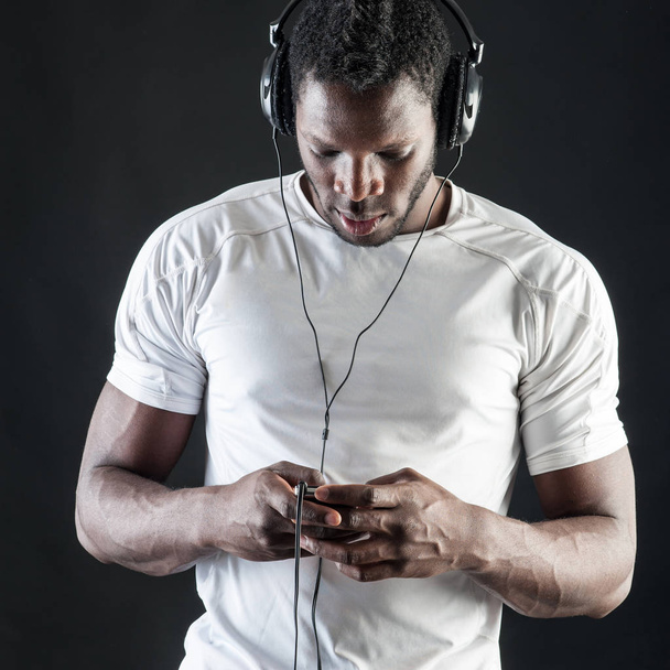 Black man listening to music with ear-phones against dark backgr - 写真・画像