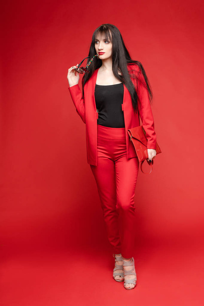 Vista lateral de morena glamorosa posando en traje rojo inteligente
 - Foto, imagen